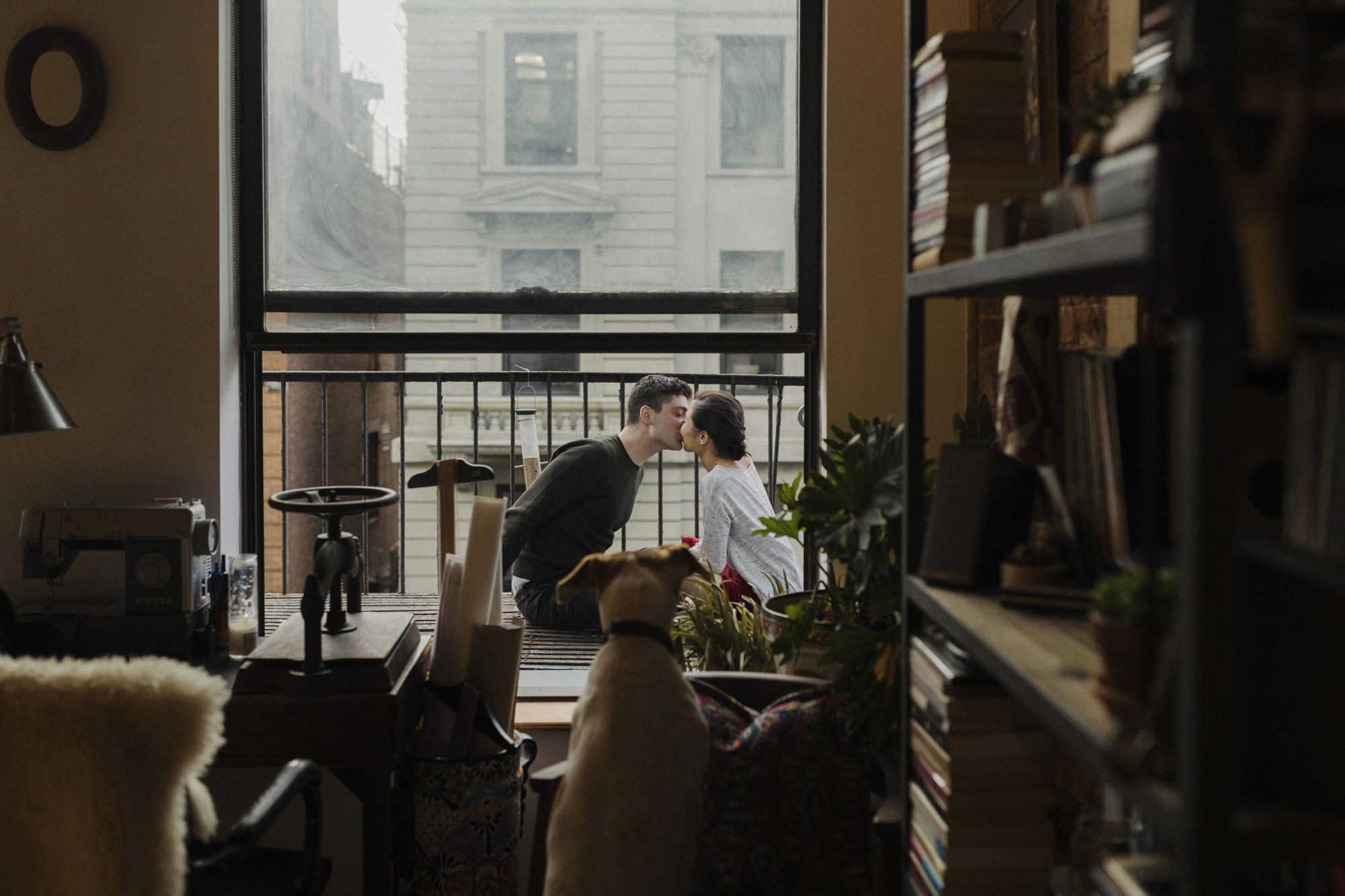Couple sitting on fire escape in Brooklyn with their dog looking out window at them